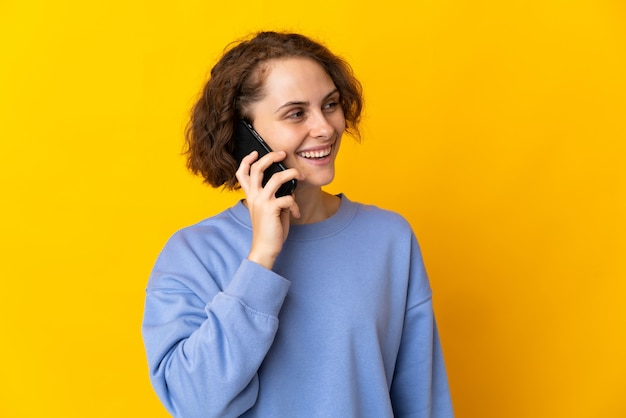 Jonge Engelse vrouw die op gele ruimte wordt geïsoleerd die een gesprek met de mobiele telefoon met iemand houdt