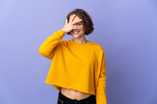 Jonge Engelse vrouw die op paarse muur wordt geïsoleerd die ogen behandelt door handen en glimlachen