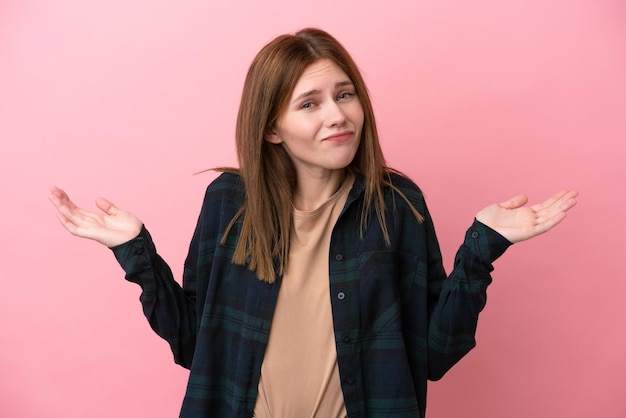 Jonge Engelse vrouw die op roze achtergrond wordt geïsoleerd die twijfels heeft terwijl het opsteken van handen