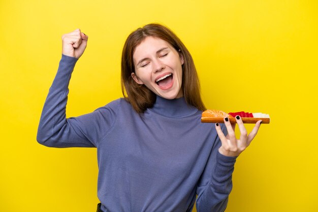 Jonge Engelse vrouw die sashimi houdt die op gele achtergrond wordt geïsoleerd en een overwinning viert