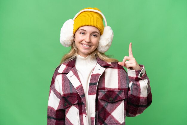 Jonge Engelse vrouw die wintermoffen draagt over een geïsoleerde achtergrond die een vinger toont en opheft als teken van het beste