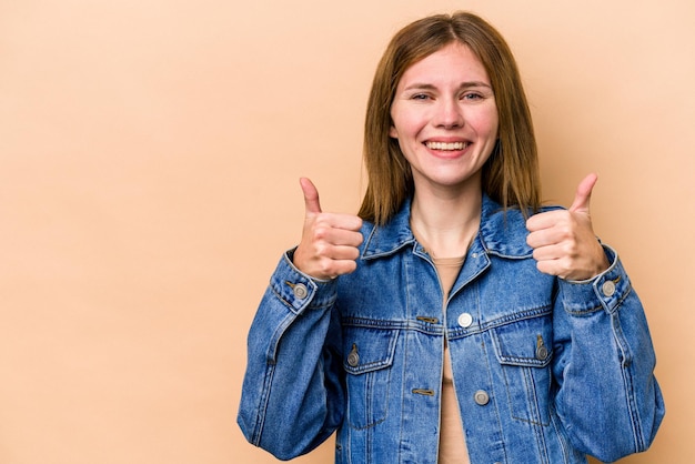 Jonge Engelse vrouw geïsoleerd op beige achtergrond glimlachend en duim omhoog