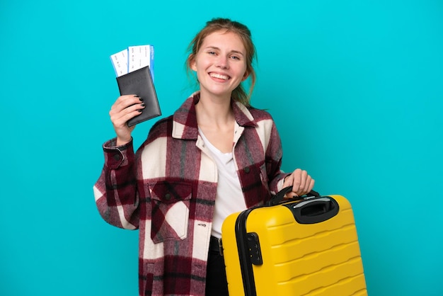 Jonge Engelse vrouw geïsoleerd op blauwe achtergrond in vakantie met koffer en paspoort