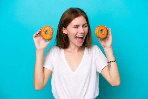 Jonge Engelse vrouw geïsoleerd op blauwe achtergrond met donuts en verrast