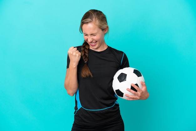 Jonge Engelse vrouw geïsoleerd op blauwe achtergrond met voetbal die een overwinning viert