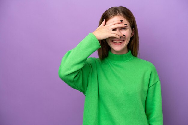 Jonge Engelse vrouw geïsoleerd op een paarse achtergrond die de ogen bedekt met de handen en glimlacht