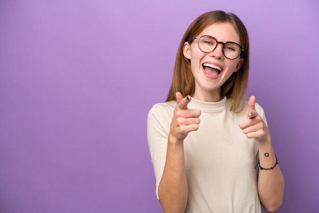 Jonge Engelse vrouw geïsoleerd op een paarse achtergrond die naar voren wijst en glimlacht