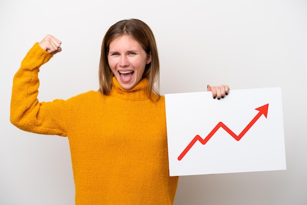 Jonge Engelse vrouw geïsoleerd op een witte achtergrond die een bord met een groeiend statistiekpijlsymbool vasthoudt en een sterk gebaar doet