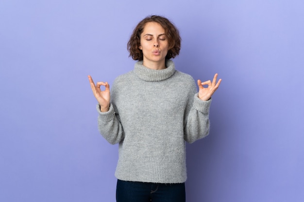 Jonge Engelse vrouw geïsoleerd op paarse muur in zen pose