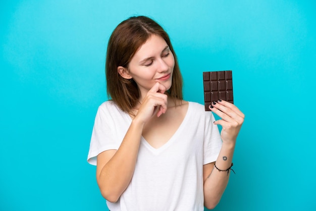 Jonge Engelse vrouw met chocola die op blauwe achtergrond wordt geïsoleerd en omhoog kijkt