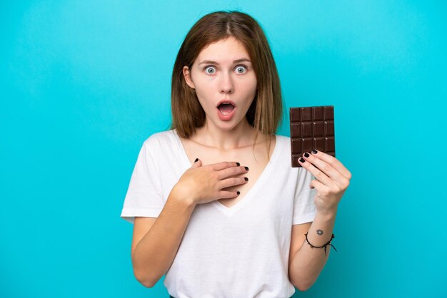 Foto jonge engelse vrouw met chocolade geïsoleerd op blauwe achtergrond verrast en geschokt terwijl ze naar rechts kijkt