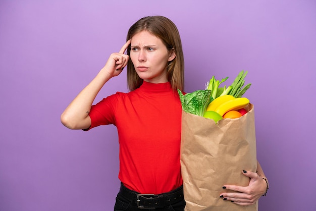 Jonge engelse vrouw met een boodschappentas geïsoleerd op een paarse achtergrond die twijfelt en denkt