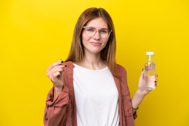 Jonge Engelse vrouw met een fles water geïsoleerd op een gele achtergrond die geld maakt gebaar