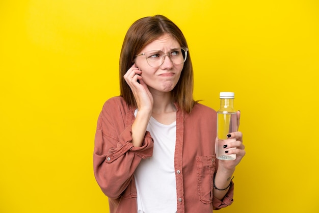 Jonge Engelse vrouw met een fles water geïsoleerd op een gele achtergrond, gefrustreerd en bedekt met oren