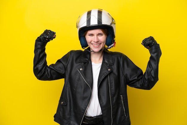 Jonge Engelse vrouw met een motorhelm die op gele achtergrond wordt geïsoleerd en sterk gebaar doet