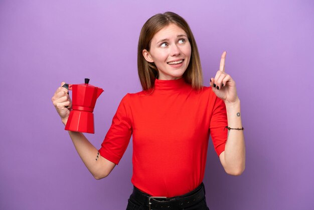 Jonge Engelse vrouw met koffiepot geïsoleerd op paarse achtergrond met de bedoeling de oplossing te realiseren terwijl ze een vinger opheft