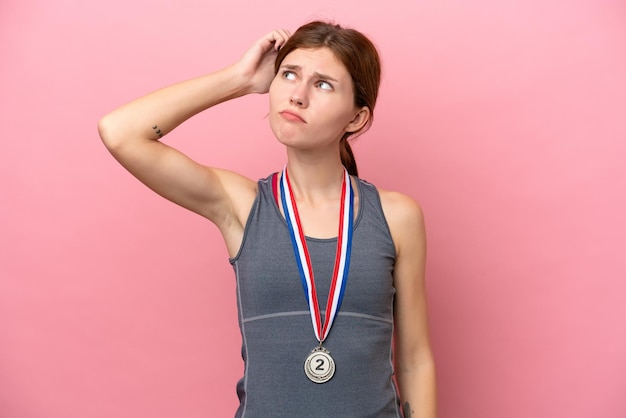 Foto jonge engelse vrouw met medailles die op roze achtergrond wordt geïsoleerd die twijfels heeft en met verwarde gezichtsuitdrukking