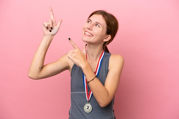 Jonge Engelse vrouw met medailles geïsoleerd op roze achtergrond wijzend met de wijsvinger een geweldig idee