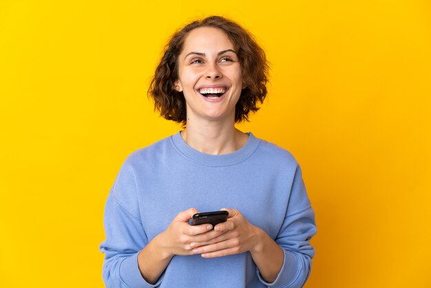 Jonge Engelse vrouw op geel die mobiele telefoon met behulp van en omhoog kijkt