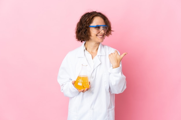 Jonge Engelse wetenschappelijke vrouw die op roze achtergrond wordt geïsoleerd die naar de kant wijst om een product te presenteren