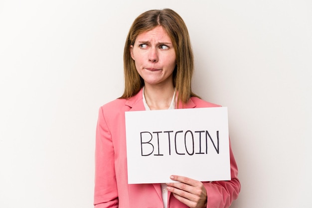 Foto jonge engelse zakenvrouw met een bitcoin plakkaat geïsoleerd op een witte achtergrond verward, voelt zich twijfelachtig en onzeker.