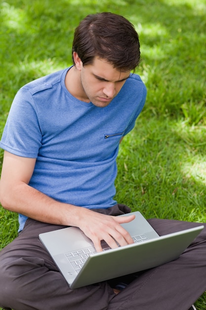 Jonge ernstige man aan het werk op zijn laptop zittend in een park