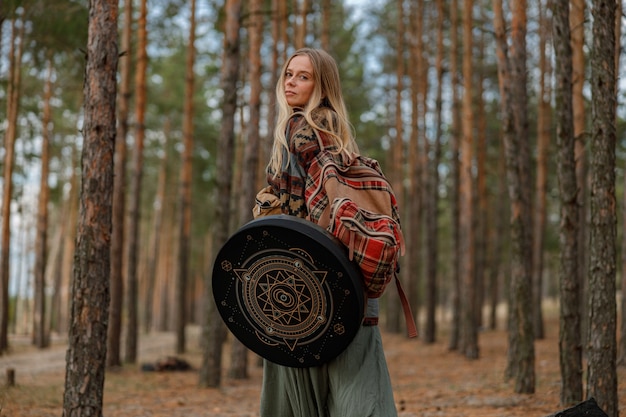 Jonge etnische volwassen sjamaan vrouw loopt en speelt meditatieve muziek op drums