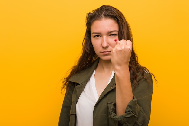 Jonge Europese die vrouw over gele achtergrond wordt geïsoleerd die vuist tonen aan camera, agressieve gelaatsuitdrukking.