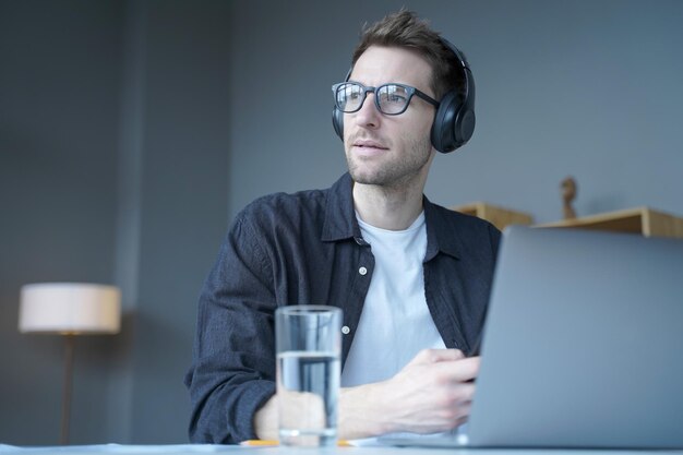 Jonge Europese man in draadloze koptelefoon luisteren naar audio podcast of kijken naar webinar op laptop