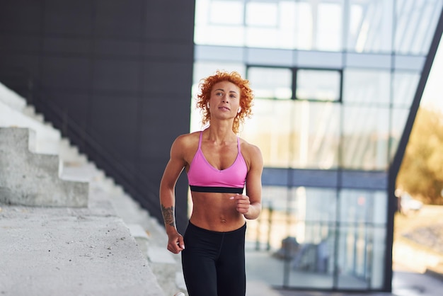 Jonge Europese roodharige vrouw in sportieve kleding die buiten loopt