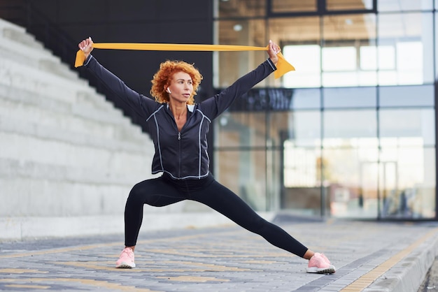 Jonge Europese roodharige vrouw in sportieve kleding doet oefeningen met touw buitenshuis