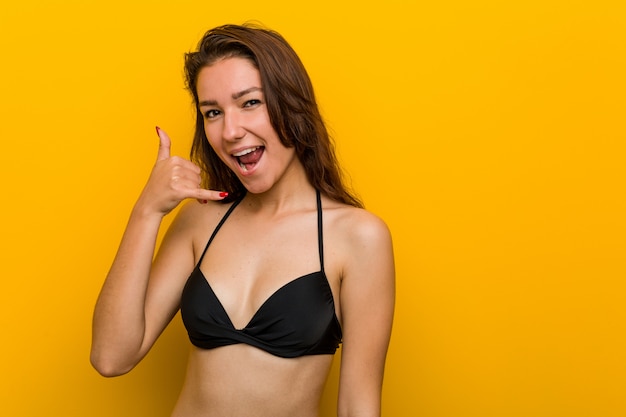 Jonge Europese vrouw die bikini draagt die een mobiel telefoongesprekgebaar met vingers toont.