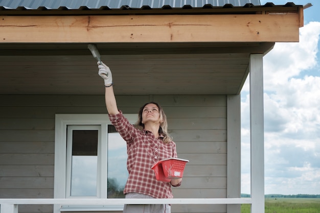 Jonge Europese vrouw die de veranda van een nieuw houten huis schildert