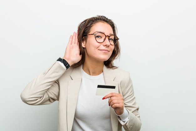 Jonge Europese vrouw die een creditcard houdt die aan een roddel probeert te luisteren.