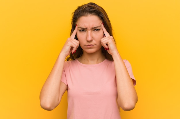 Jonge europese vrouw geïsoleerd over gele ruimte gericht op een taak, met haar wijsvingers hoofd wijzend.