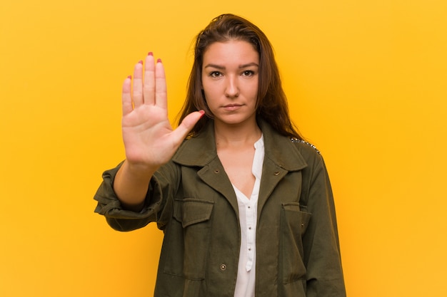 Jonge Europese vrouw over gele muur die zich met uitgestrekte hand bevindt die eindeteken toont, dat u verhindert.