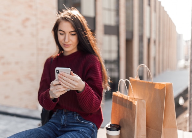 Jonge Europese vrouw zitten met koffiekopje asmartphone en boodschappentassen