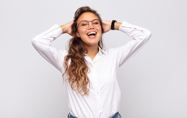 jonge expressieve vrouw met bril en elegante witte blouse poseren op witte muur