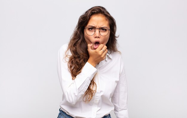 jonge expressieve vrouw met bril en elegante witte blouse poseren op witte muur