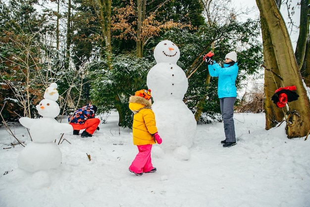 Jonge familie bouwt sneeuwpop in het besneeuwde park, klein peutermeisje helpt