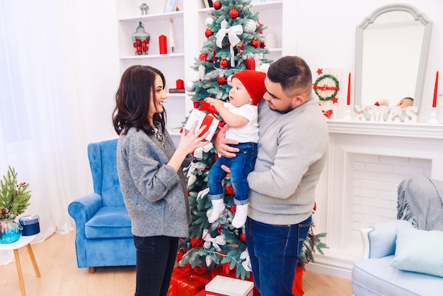 Jonge familie geeft de eerste kerstcadeau doos aan hun pasgeboren kind. Peuterjongen ontvangt zijn eerste kerstcadeau.