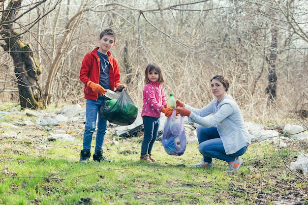 Jonge familie moeder met twee kinderen vrijwilligers maken het lentepark schoon, verzamelen afval en plastic flessen