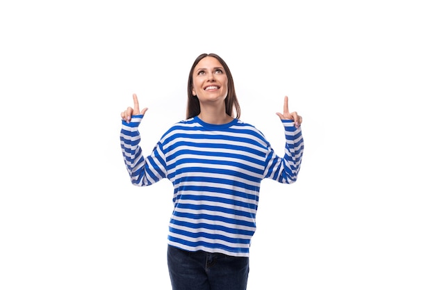 Jonge fashionista brunette vrouw gekleed in een gestreepte blauwe sweatshirt wijst haar handen omhoog