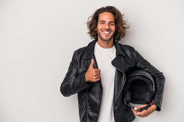 Jonge fietser blanke man met een motorhelm geïsoleerd op een grijze achtergrond glimlachend en duim omhoog