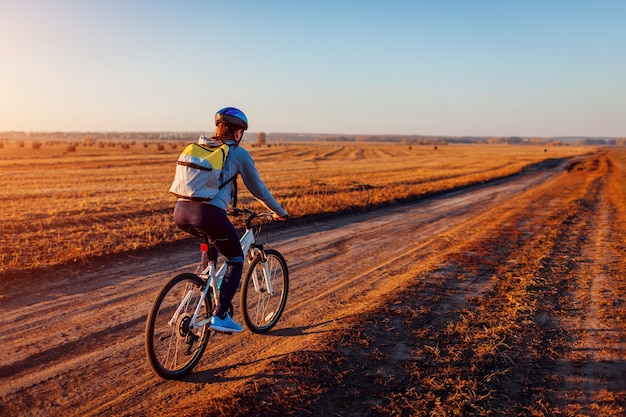 Jonge fietser rijden in herfst veld met hooibergen bij zonsondergang. Vrouw die met rugzak op fiets reist. Gezonde levensstijl.