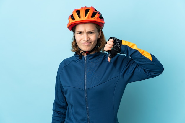 Jonge fietser vrouw geïsoleerd op blauw met duim omlaag met negatieve uitdrukking
