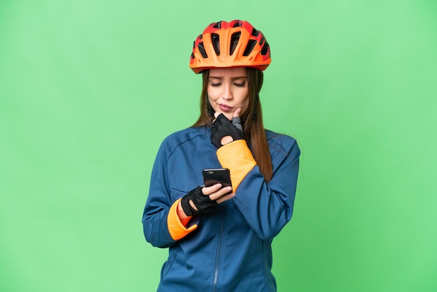 Jonge fietser vrouw over geïsoleerde chroma key achtergrond denken en een bericht verzenden