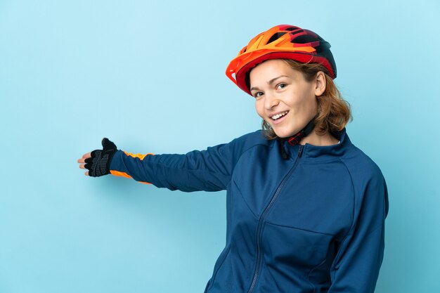 Jonge fietservrouw die op blauwe achtergrond wordt geïsoleerd die handen aan de kant uitbreidt om uit te nodigen om te komen