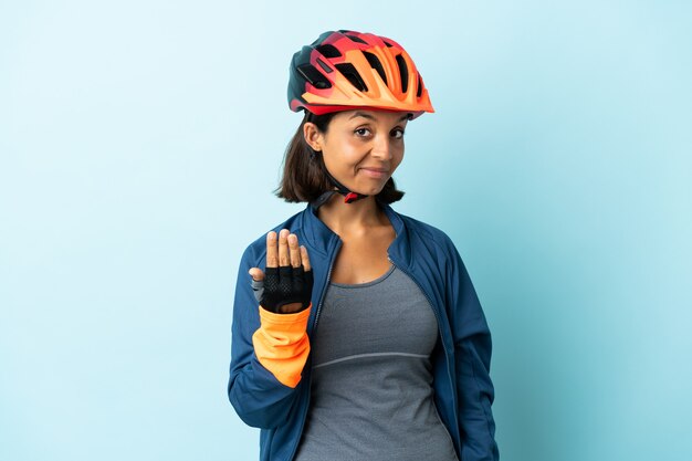 Jonge fietservrouw die op blauwe achtergrond wordt geïsoleerd die uitnodigt om met hand te komen. Blij dat je gekomen bent