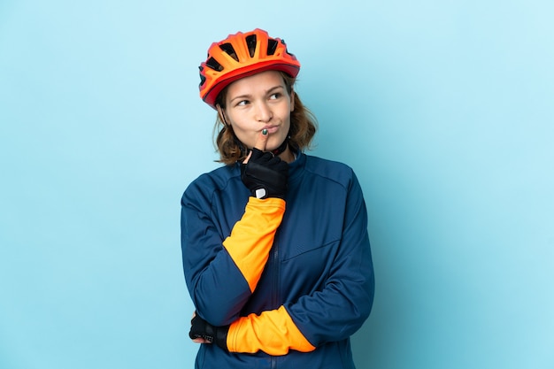 Jonge fietservrouw die op blauwe muur wordt geïsoleerd die twijfels heeft tijdens het kijken